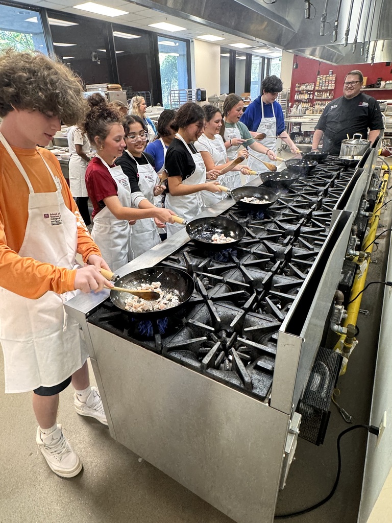 Students standing over a frying pan on a stove in a culinary arts classroom practicing cooking skills.