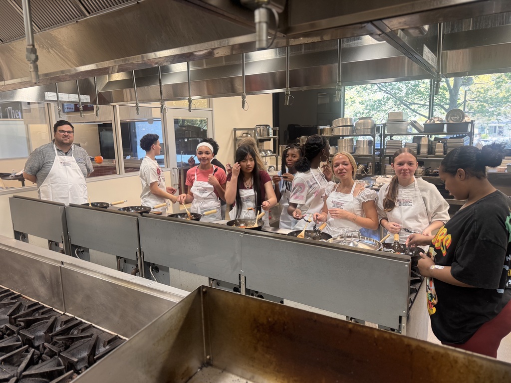 Students smiling for the camera while cooking their food.