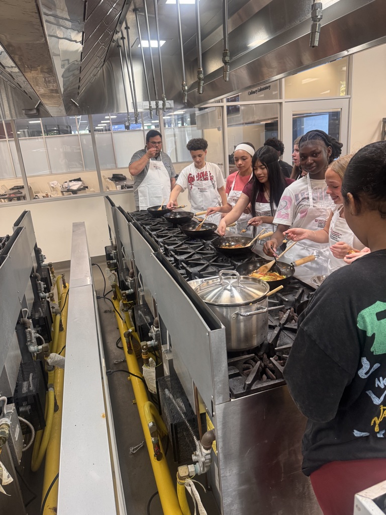 Students standing over frying pans cooking.