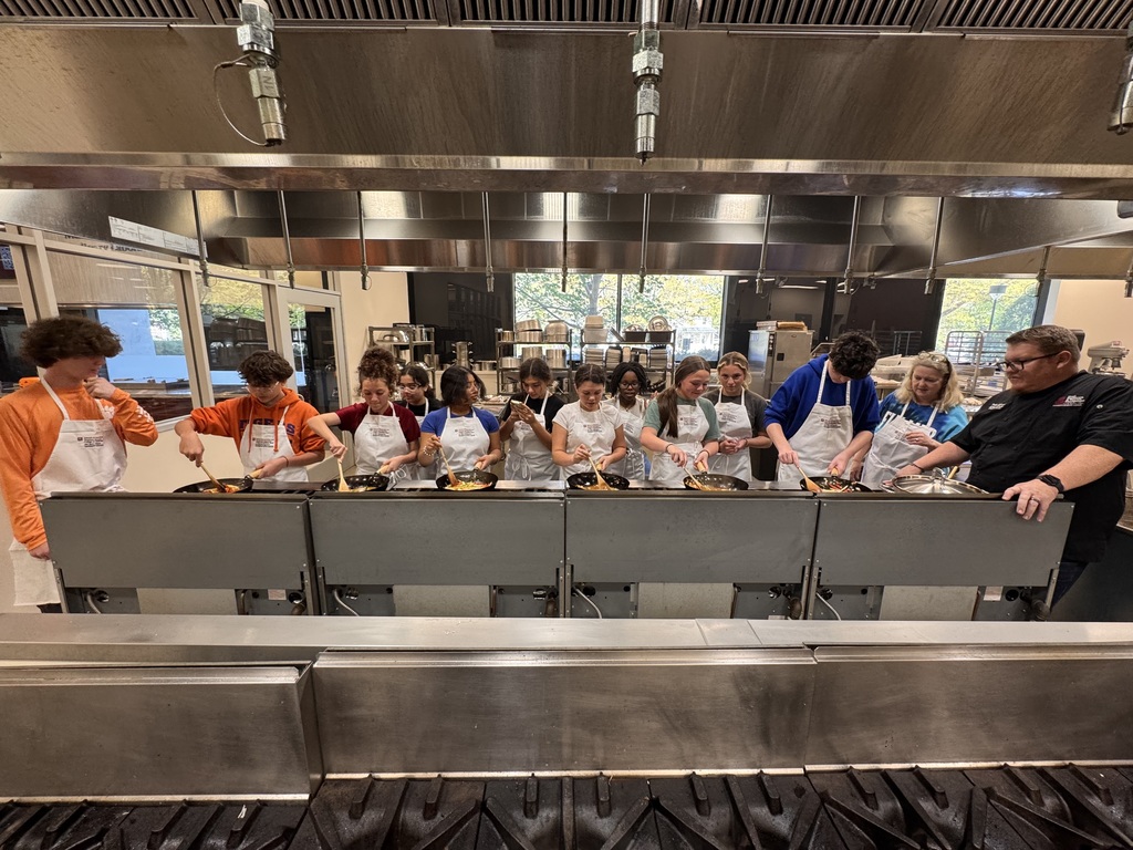 Students standing over a frying pan on a stove in a culinary arts classroom practicing cooking skills.