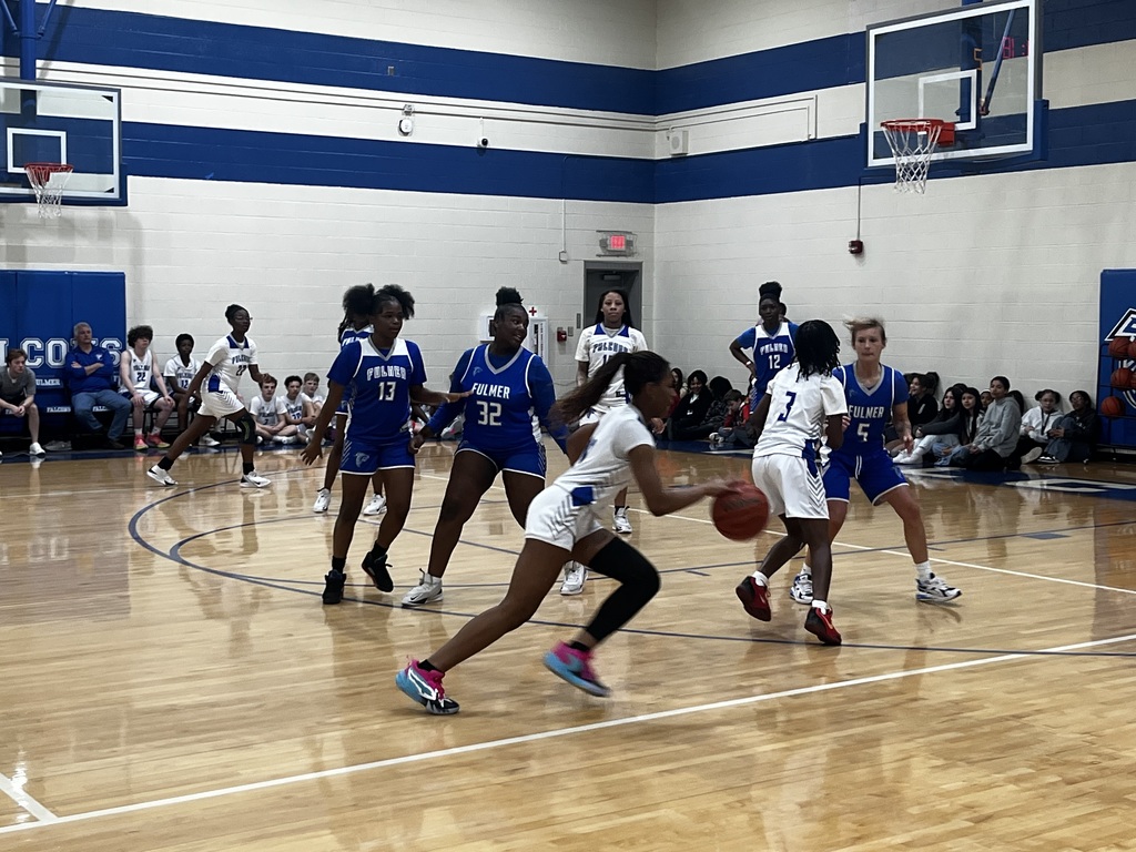 A female student dribbles the basketball towards the goal.