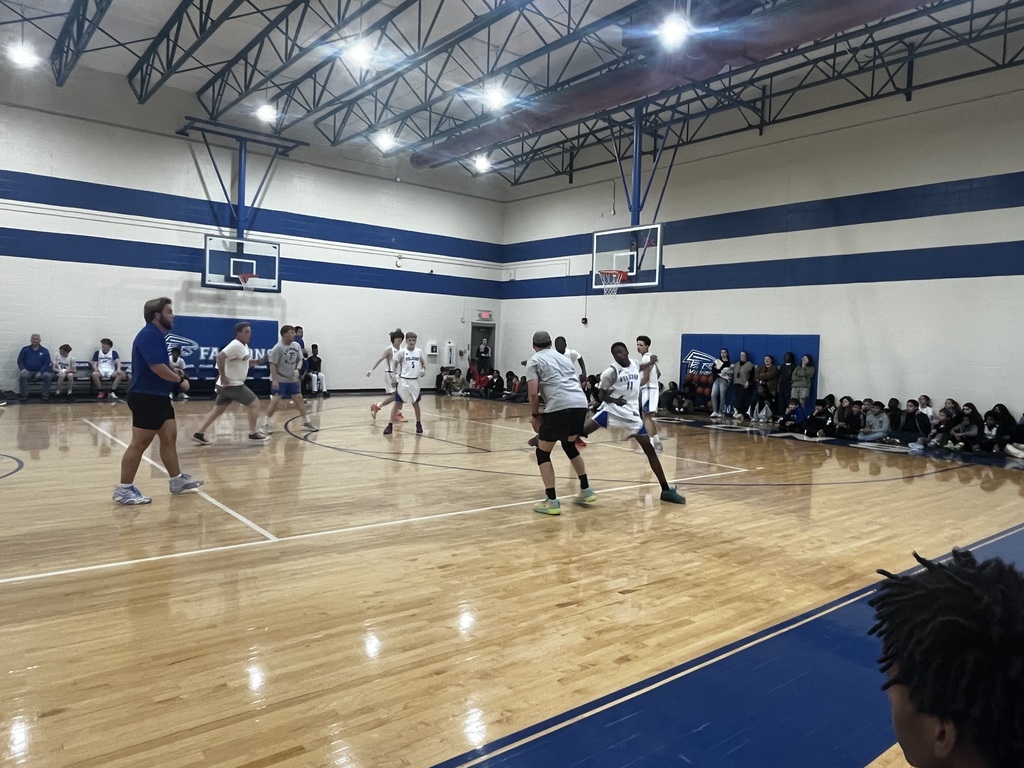 Boys play basketball on the court. One teacher is shown waiting for the ball to be passed to him while others run on the court.