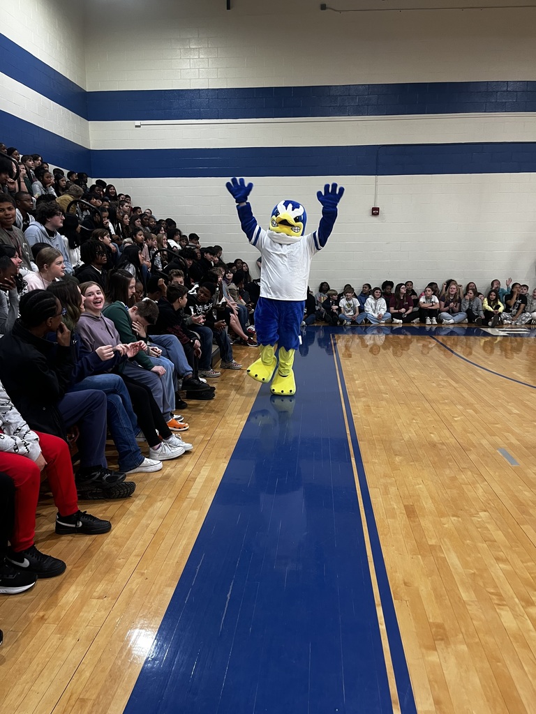 Freddie the Falcon has his arms up in the air in front of students sitting in the stadium seats awaiting the game.