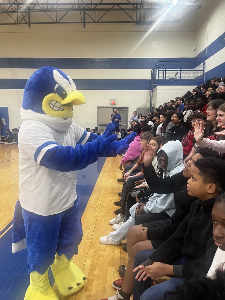 Freddie the Falcon high fives students sitting in the gym stands.