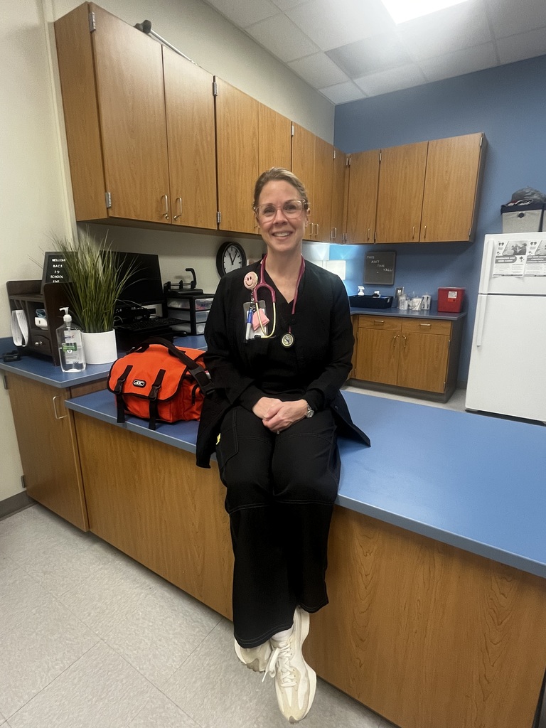 School Nurse Julie McCurdy smiles for teh camera while sitting on the counter in her nurse's office.