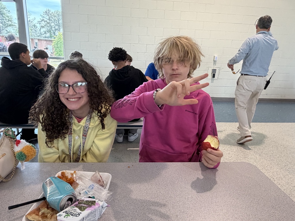 A female and male student smile for the camera sitting at a cafeteria table during lunch.