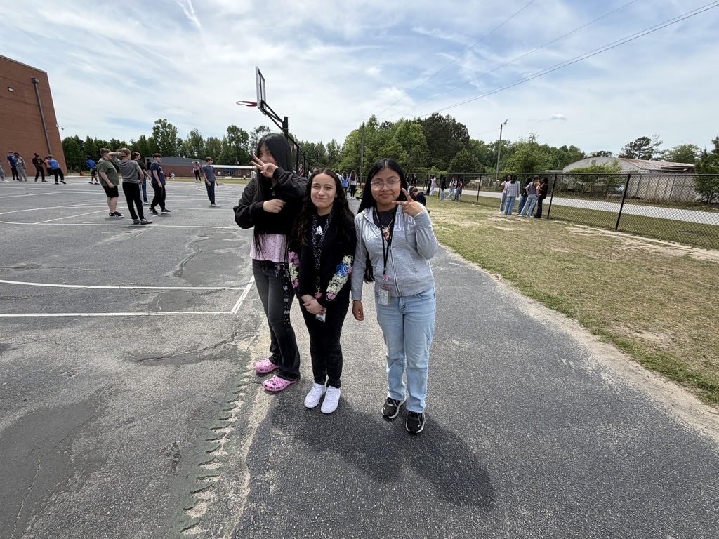 Three students smile for the camera while standing on the blacktop outside during recess.