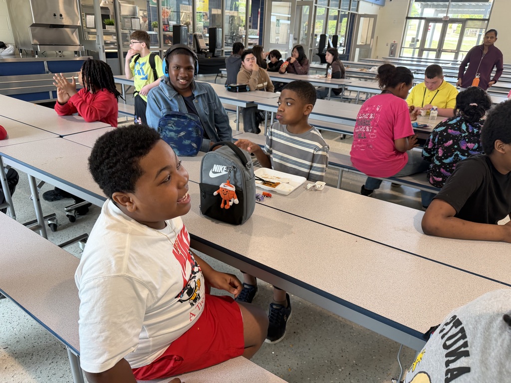 Students sit at the cafeteria table looking at the camera.