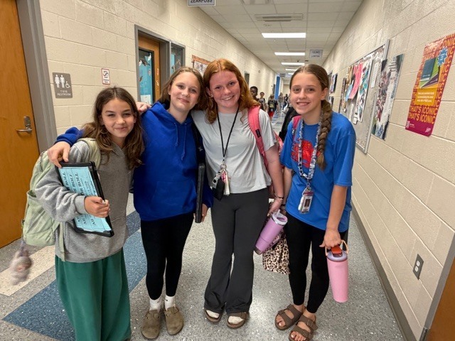 Four girls stand together in the hallway smiling at the camera.