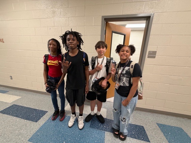 Two girls and two boys stand in the hallway and smile for the camera.
