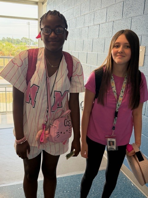 Two girls stand side by side in the hallway at the top of the stairs smiling at the camera.