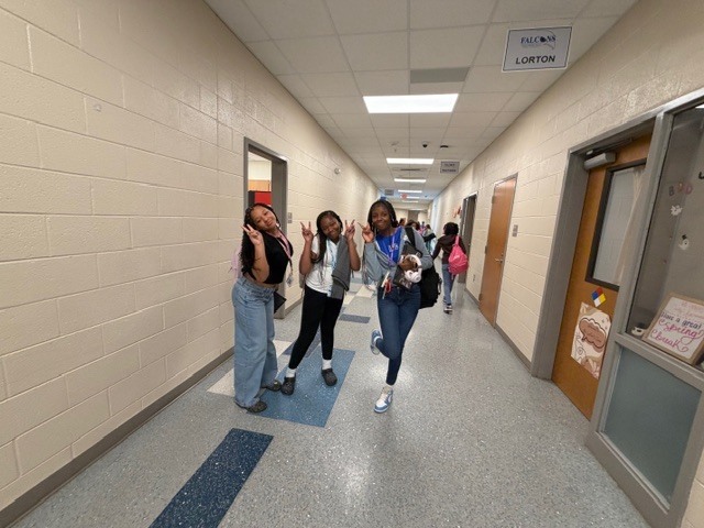 Three girls pose for the camera holding up peace signs and smiling in the hallway.