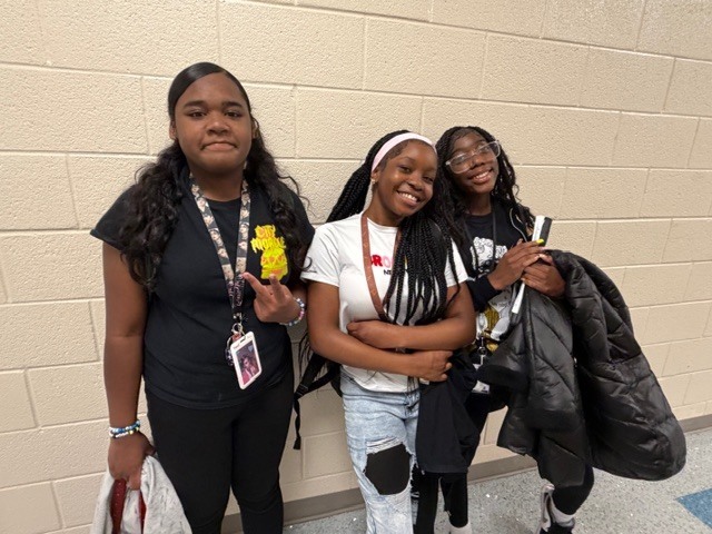 Three girls stand together in the hallway and smile for the camera.