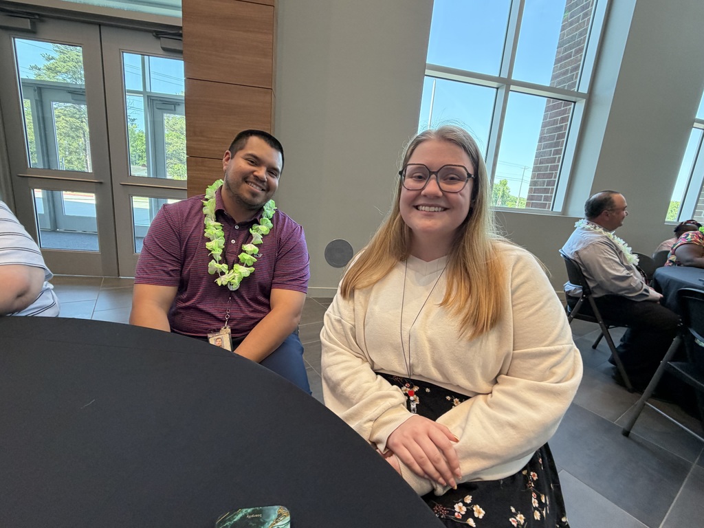 A male and female teacher sit at a table and smile at the camera.