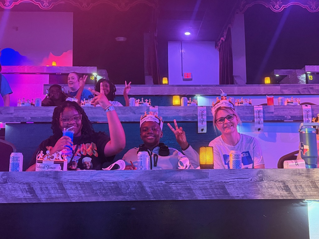 Students seated at tables waiting for the Medieval Times Show to begin. Three students are holding peace signs in the air.