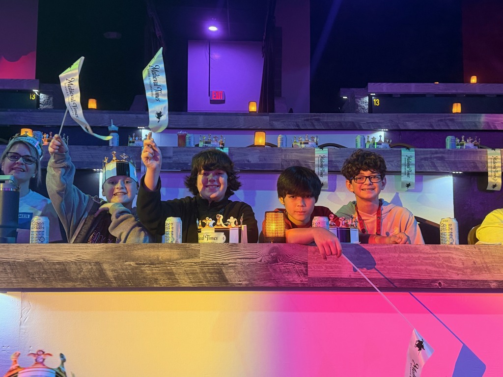 Students seated at tables waiting for the Medieval Times Show to begin. Two students hold up the Medieval Times flags.