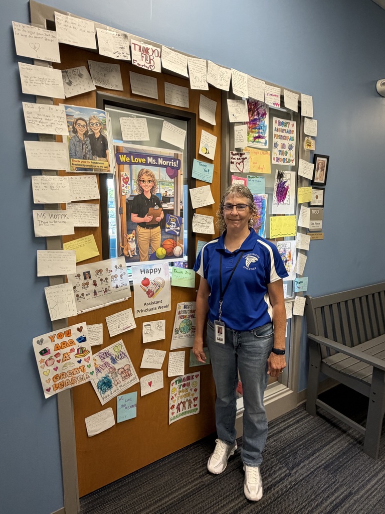 The assistant principal smiles and stands next to her office door with notes from students and posters to celebrate her for National School Principals Month.