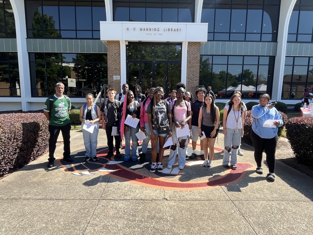 A group of students stand outside in front of a building at Claflin University. They are looking at the camera and smiling.