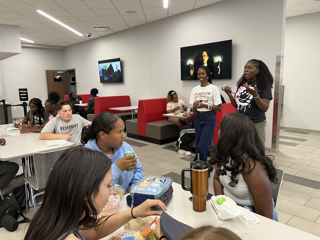 A group of students sit and eat in Claflin's cafeteria and listen to two Clafin University students talk with them.