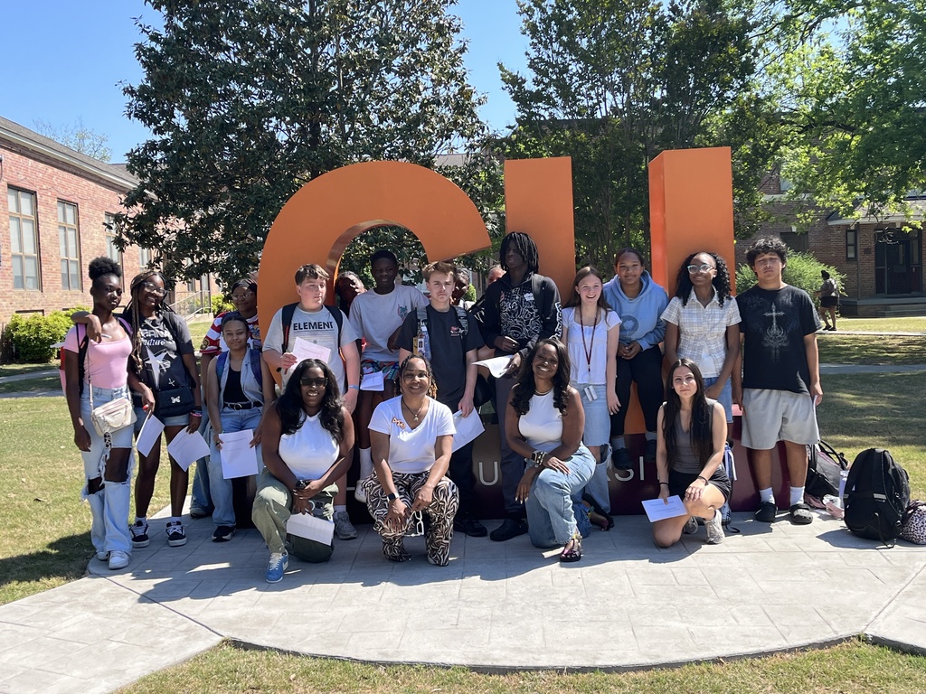 A group of students stand outside in front of large CU letters that stands for Claflin University. They are looking at the camera and smiling.