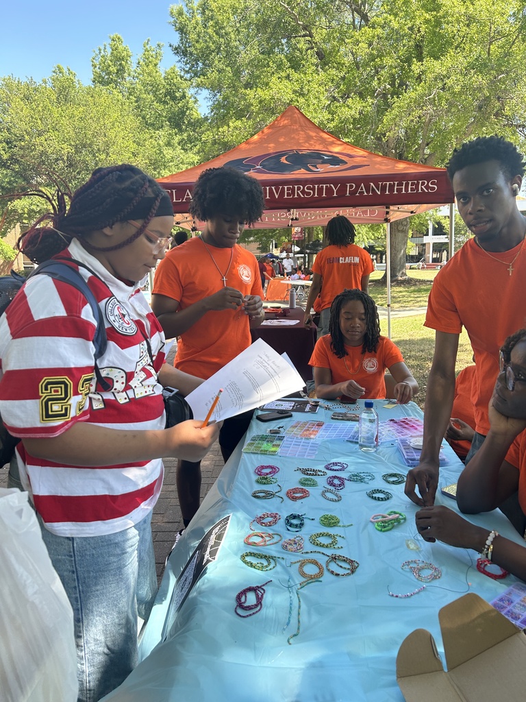 A group of students from middle school talk outside with  Clafin University Students at a table outside.