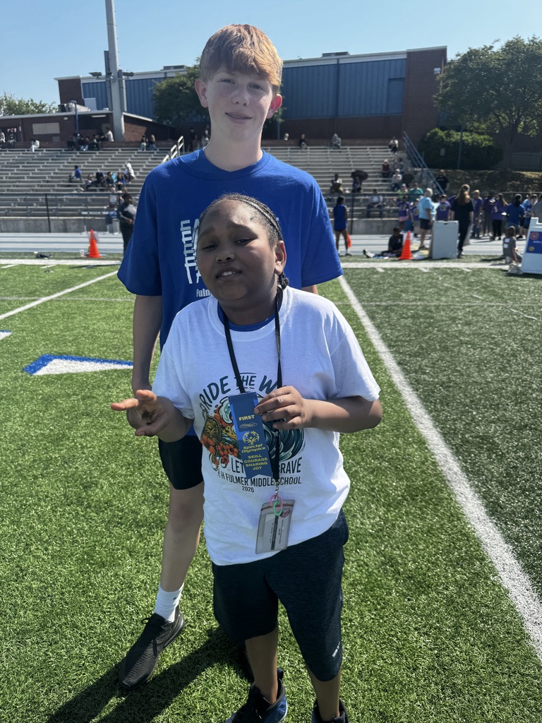 One student stands behind another student and both are looking at the camera.