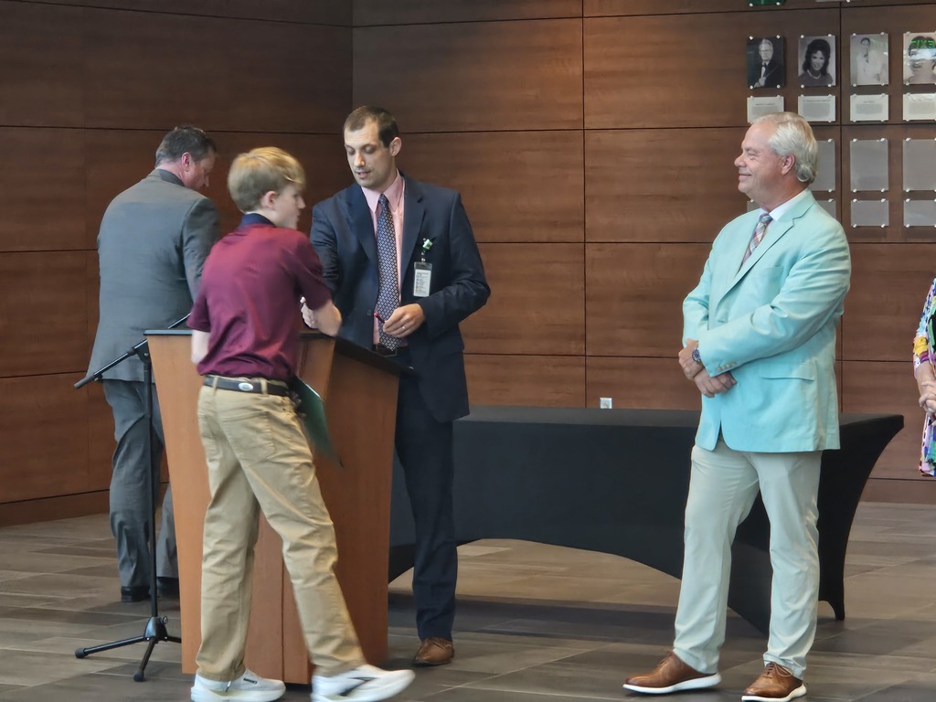 A student is shown shaking hands with a district employee who is standing at a podium.