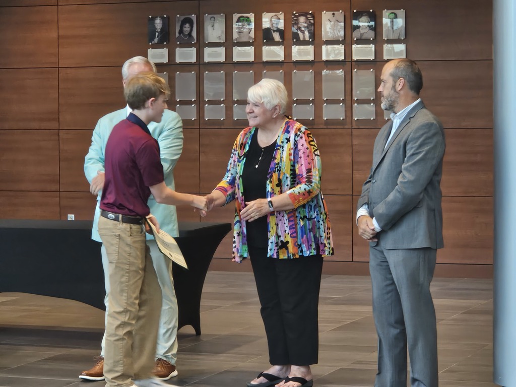 A student is shown shaking hands with a board member. Other board members are shown standing side by side.