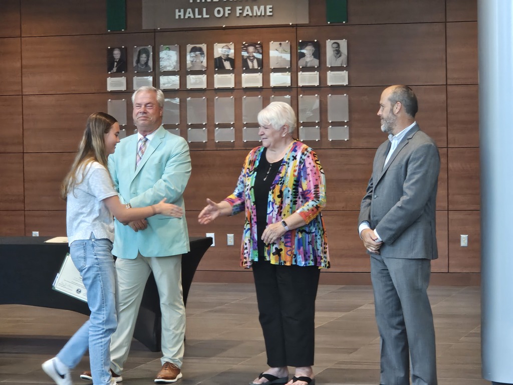 A student is shown shaking hands with a board member. Other board members are shown standing side by side.