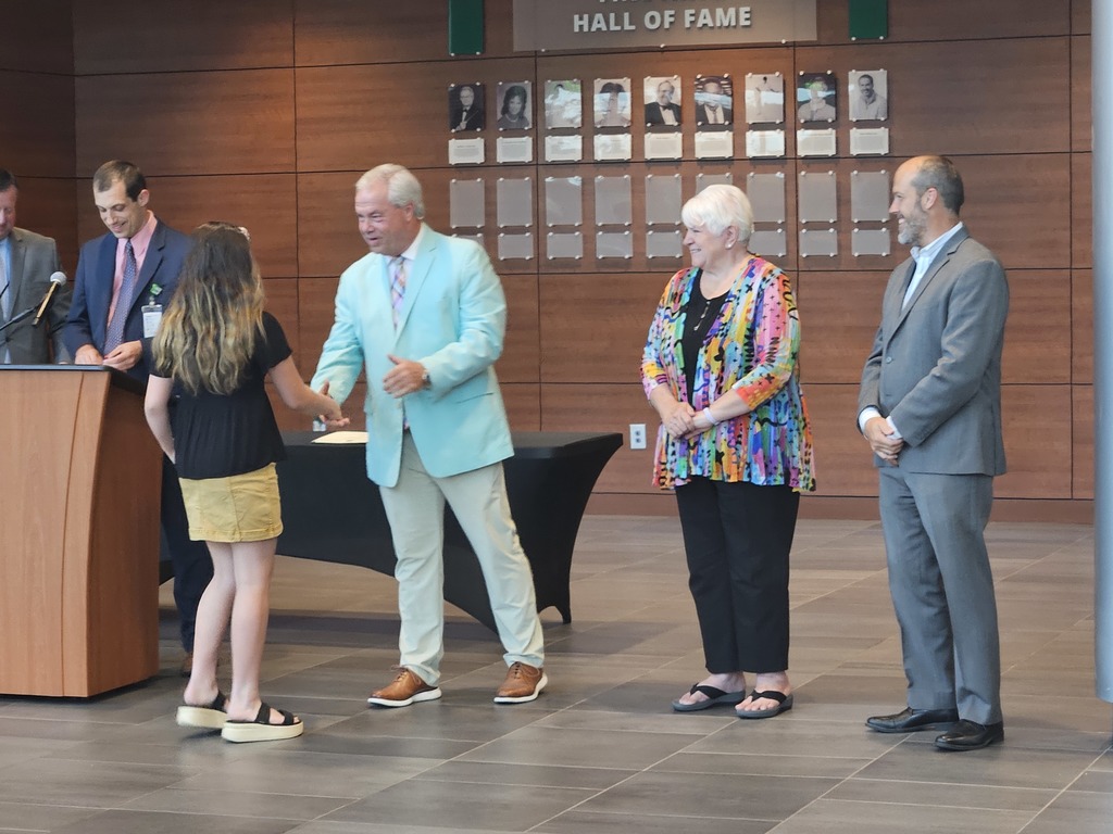 A student is shown shaking hands with a board member. Other board members are shown standing side by side.