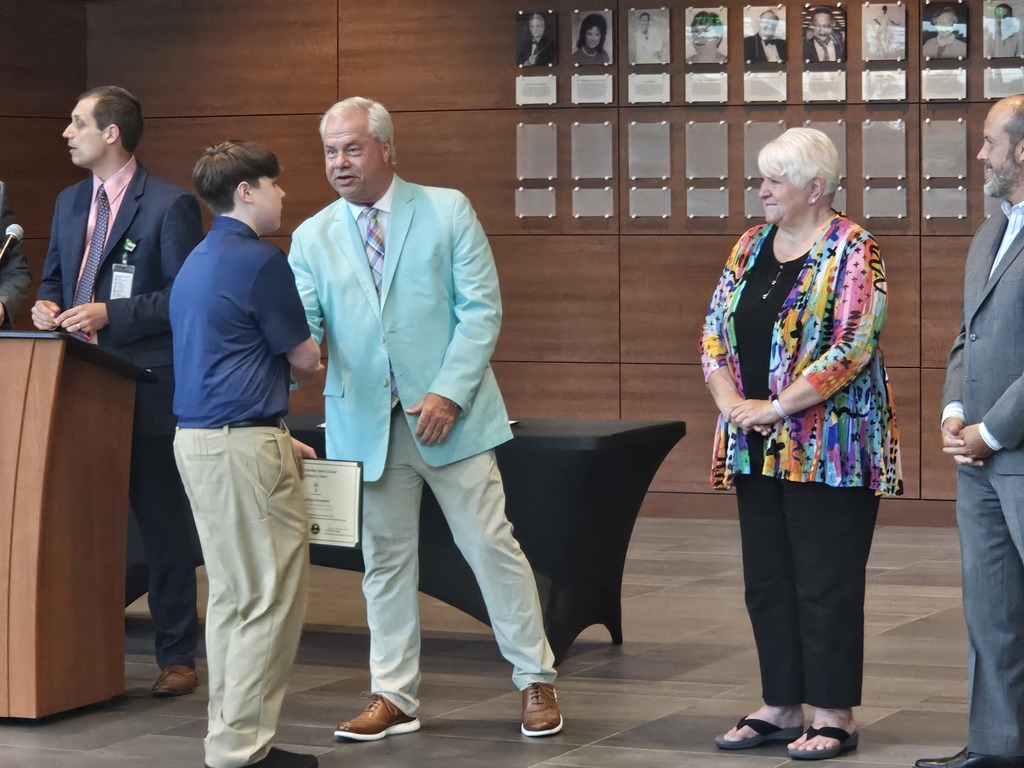 A student is shown shaking hands with a board member. Other board members are shown standing side by side.