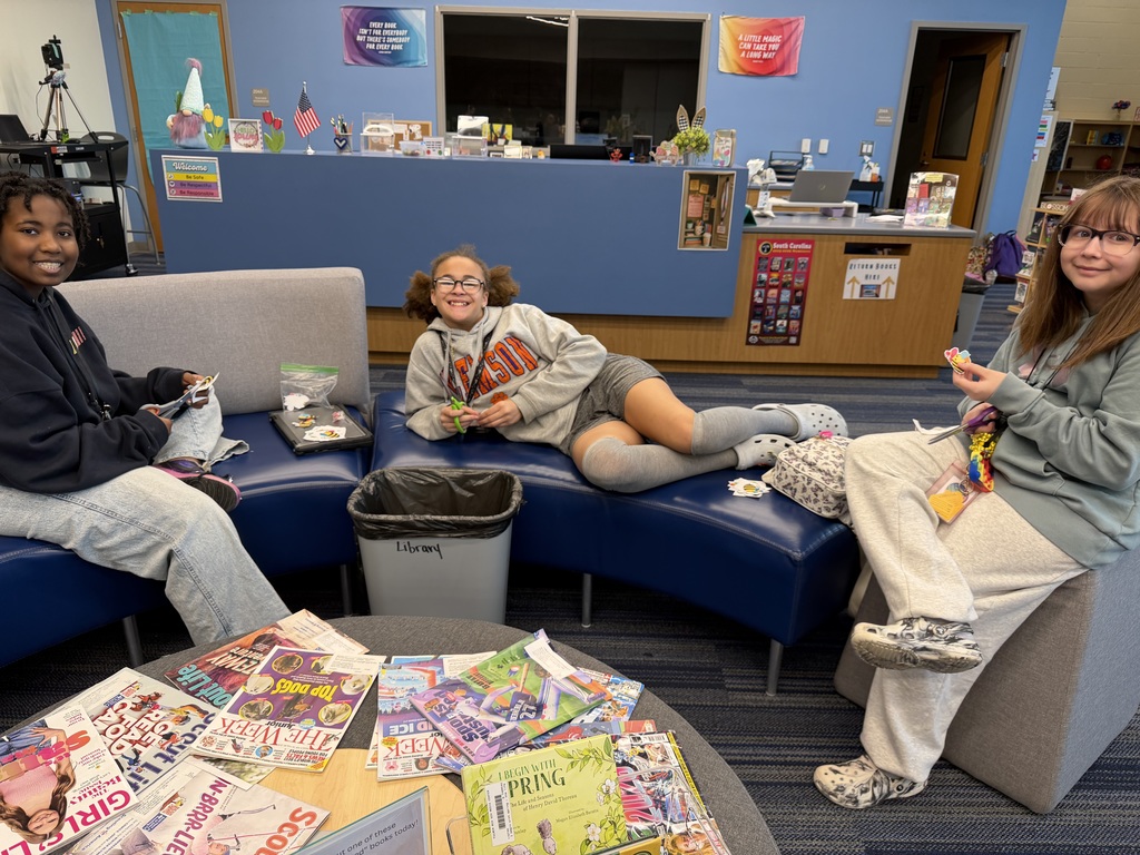 Three students sit on the couch in the library while cutting out bumblebees to use with the new scavenger hunt in the library.