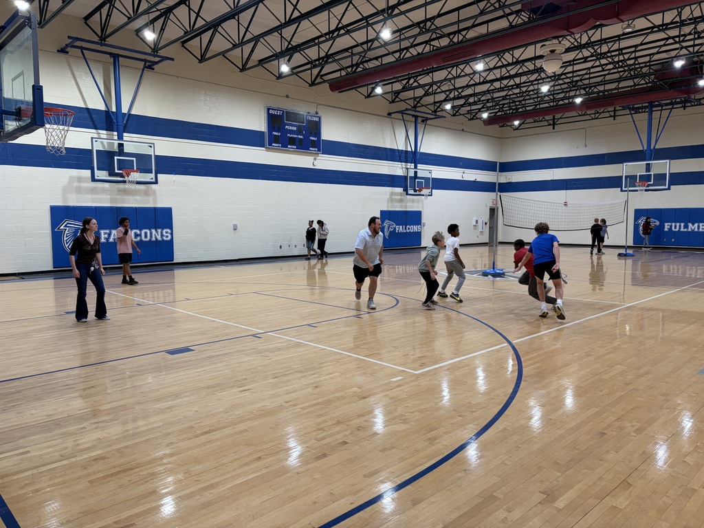 Coach McGee is shown running with male students up the gym court playing basketball.