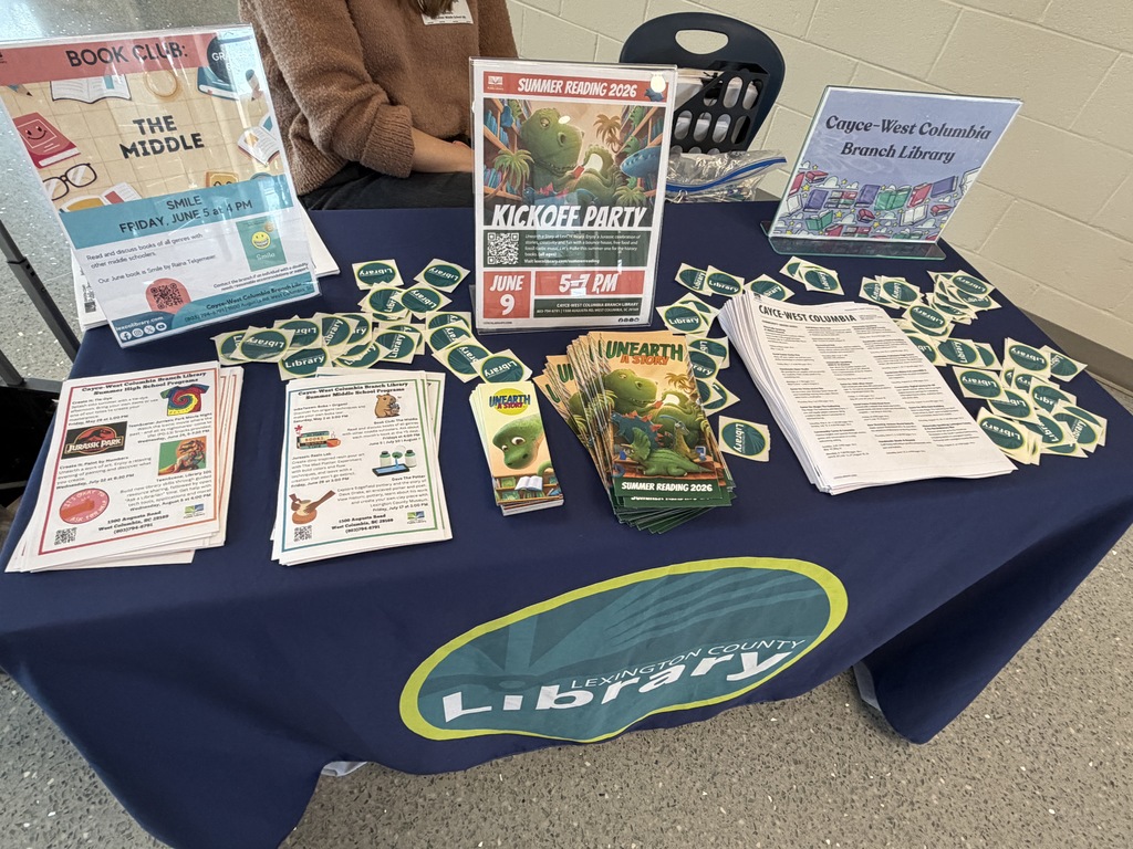 There is a table filled with papers, brochures, bookmarks, Library stickers, and signs related to the Lexington County Public Library system and the summer reading programs and summer events held at the library.