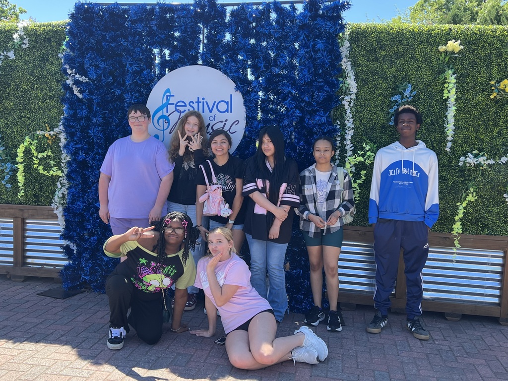 A group of students stand in front of a backdrop with a white circle on the backdrop stating "Festival of Music."