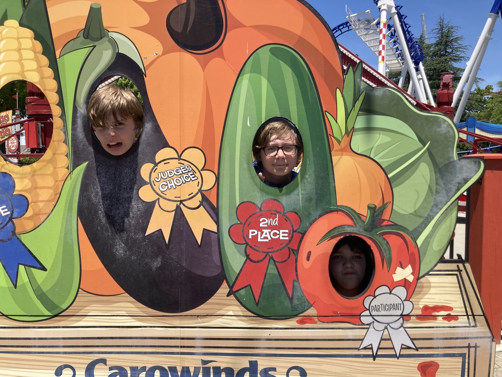 Three students show their faces through a display of vegetables that have ribbons on them labeled "Judges Choice,"  "2nd Place," and "Participant."