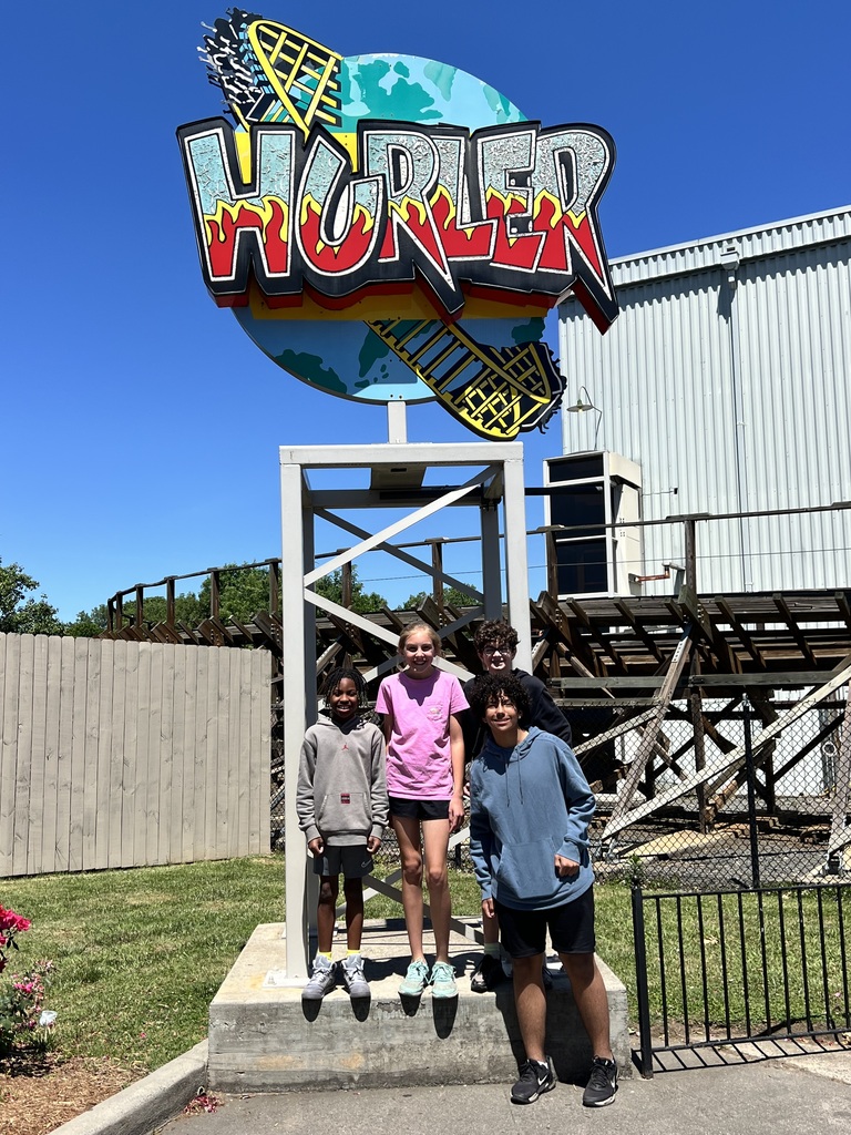 Four students stand in front of a large sign with the rides name "Hurler" in bold letters in front of planet Earth.
