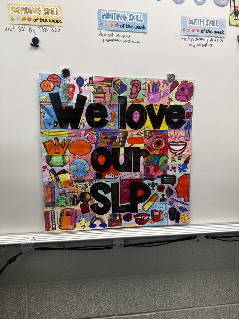 A large sign is magnetic clipped to the board in a classroom.  The sign is a large collage of illustrated and colored  pictures colored by students that form together when taped. In large bold letters on this sign it states, "We love our SLP"
