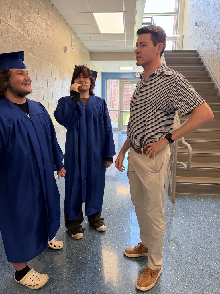 Two senior graduates talk to their once math teacher in the hallway.
