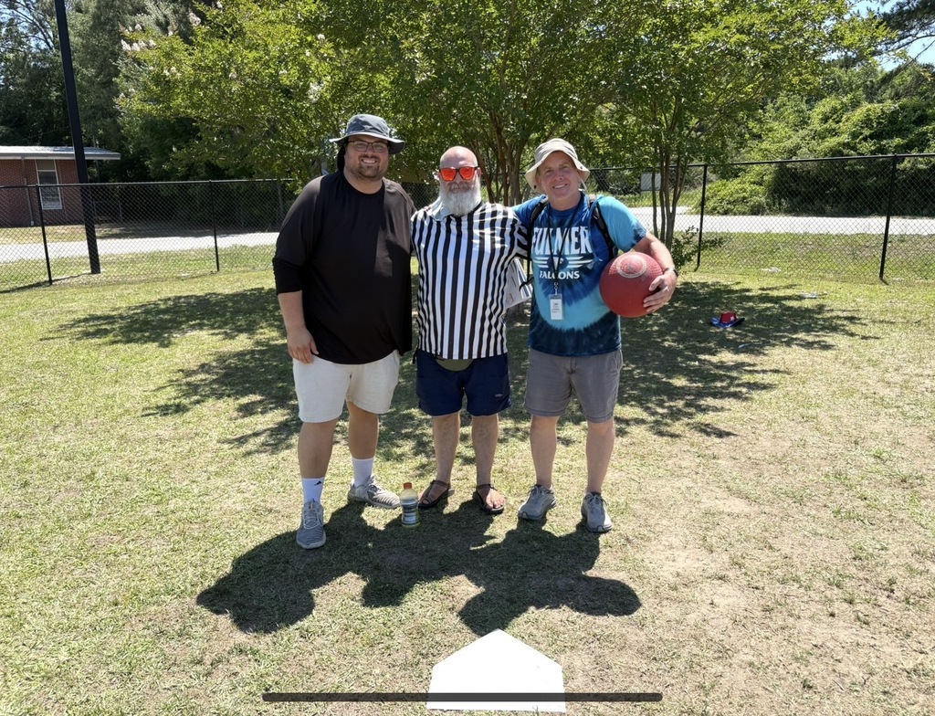 Three umpires for the kickball tournament stand together outside after the tournament and smile for the camera. They are all teachers.