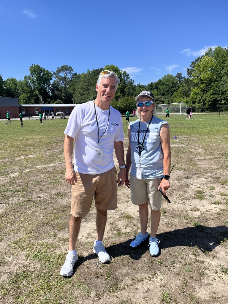 Two administrators stand together during the kickball tournament outside and smile at the camera.