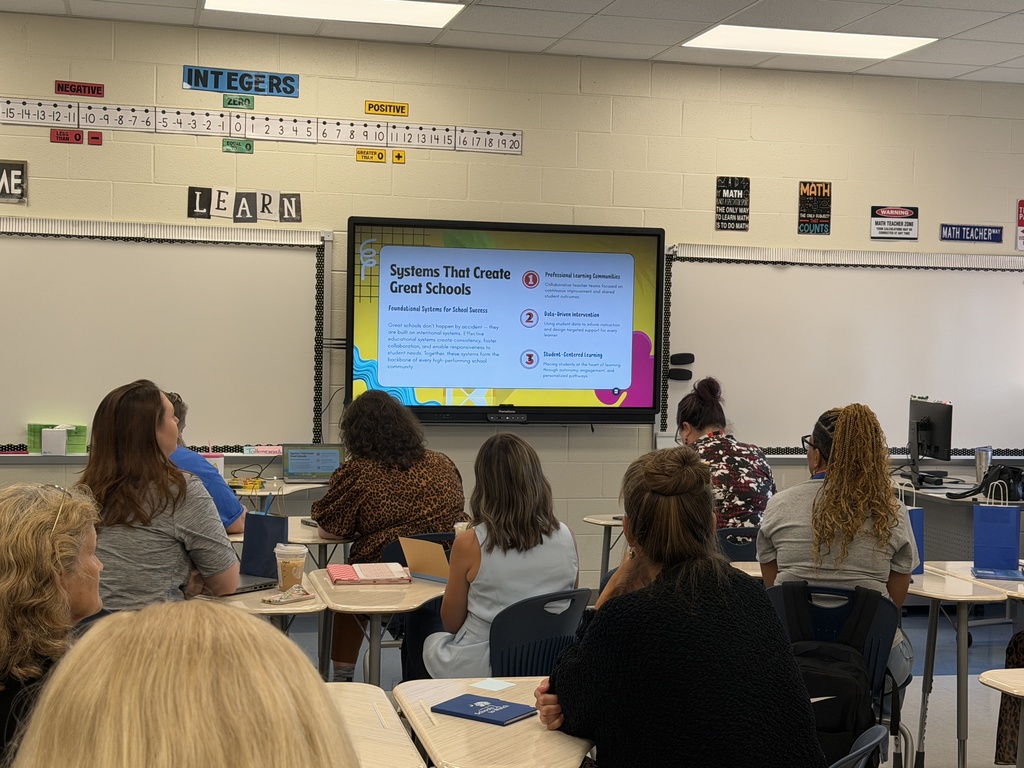 Two faculty members from Fulmer are shown in a photo with other educators from across the state; all of their backs are turned towards the camera as everyone is looking at the Promethean board with information on it that is titled "Systems That Create Great Schools."