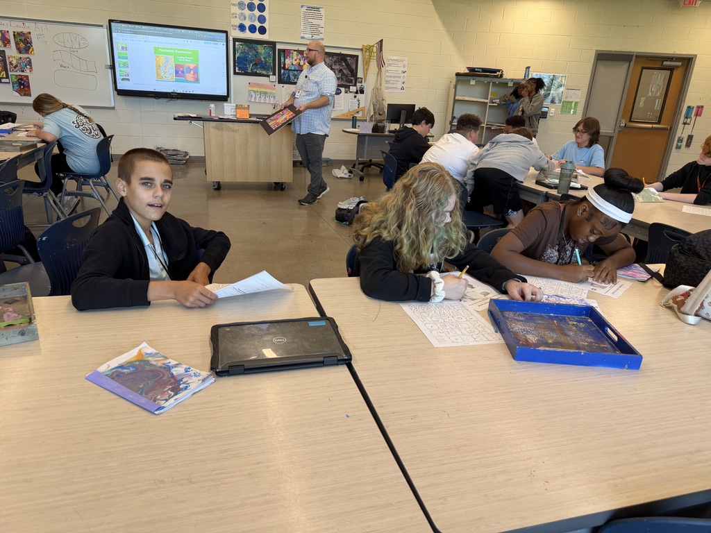 Students sit at a table in art class working on brainstorming their psychedelic drawings while and after viewing previous students' psychedelic artwork.
