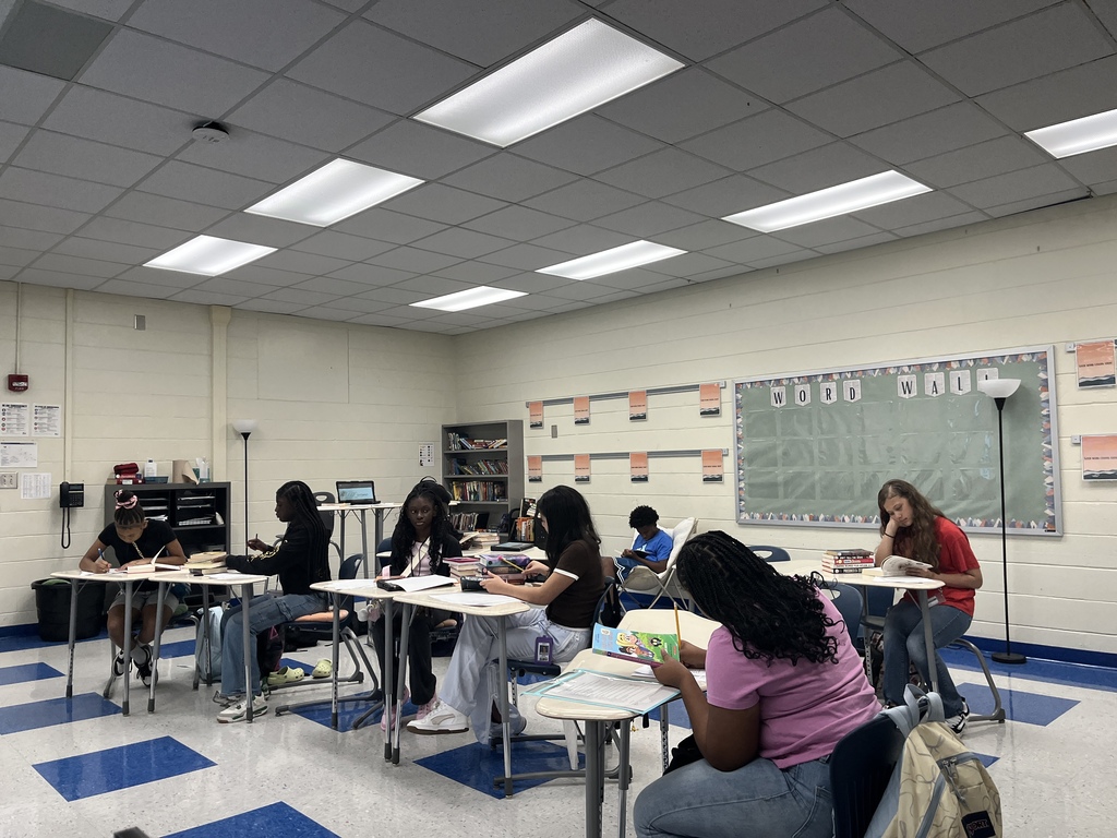Students are seated at their desks in a classroom either completing a reading interest survey or reading parts of books to find out if they would enjoy reading them or not. Students were able to check out books they wanted from Ms. Lane's classroom library.
