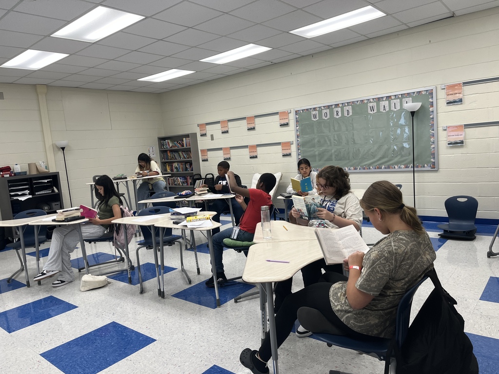 Students are seated at their desks in a classroom either completing a reading interest survey or reading parts of books to find out if they would enjoy reading them or not. Students were able to check out books they wanted from Ms. Lane's classroom library.