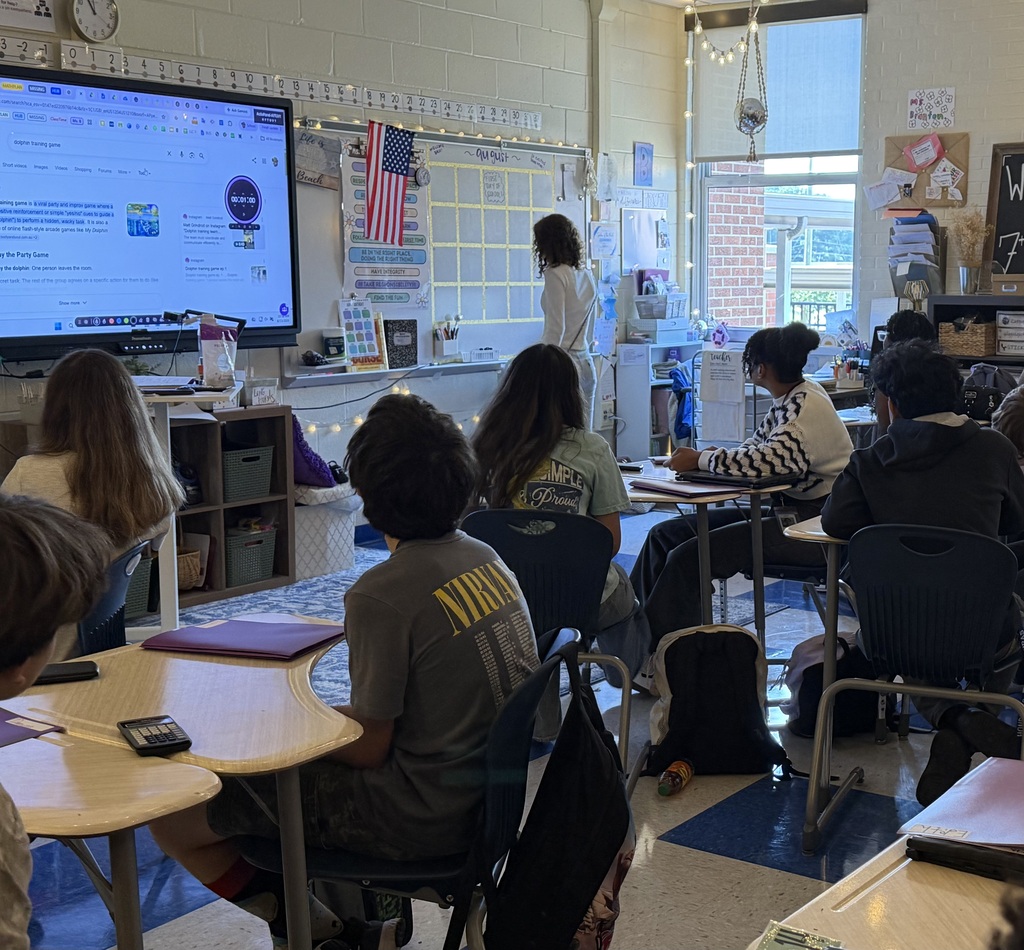 Ms. Branton's class also got to participate in "Dolphin Training" in her classes the other day. Her students discussed the importance of providing feedback to the "Dolphin" so they could learn faster. They could only provide feedback if the "Dolphin" participated in the game! Similar to how important it is to try in math so that Ms. Branton can provide feedback to work towards mastery!  A student is shown standing facing the board asking as the Dolphin, and other students are seated in their desks giving the Dolphin instructions to provide feedback.