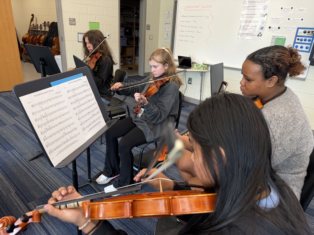 Students are seated in their chairs during 8th grade Orchestra classes with their instruments held in position and practicing The Star-Spangled Banner piece in preparation for the upcoming Veteran's Day Assembly.