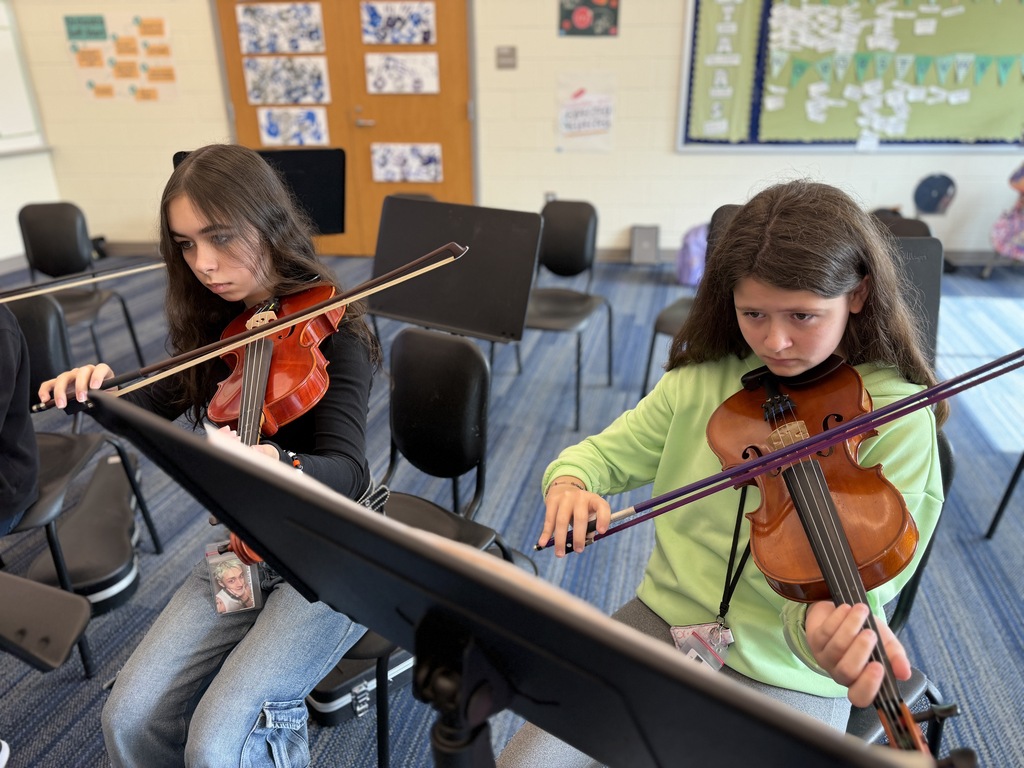 Students are seated in their chairs during 8th grade Orchestra classes with their instruments held in position and practicing The Star-Spangled Banner piece in preparation for the upcoming Veteran's Day Assembly.