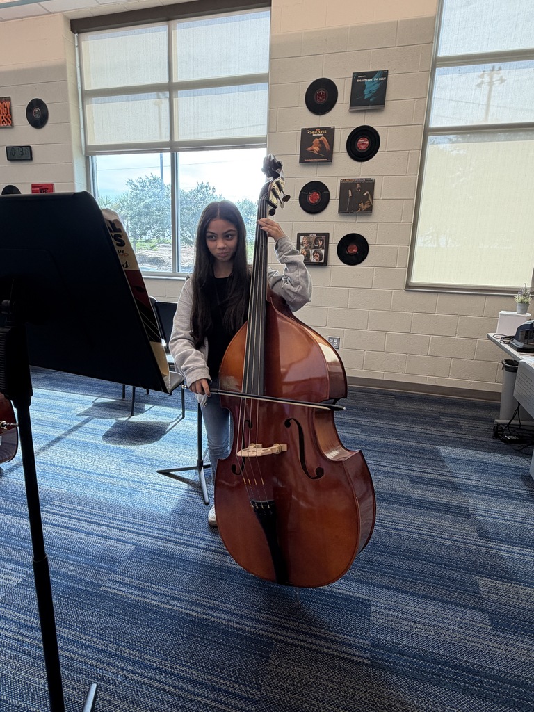 A student is shown holding her cello and the bow is in her hands held over the strings. She is looking at the sheet music on the music stand.