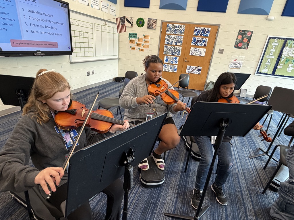 Students are seated in their chairs during 8th grade Orchestra classes with their instruments held in position and practicing The Star-Spangled Banner piece in preparation for the upcoming Veteran's Day Assembly.